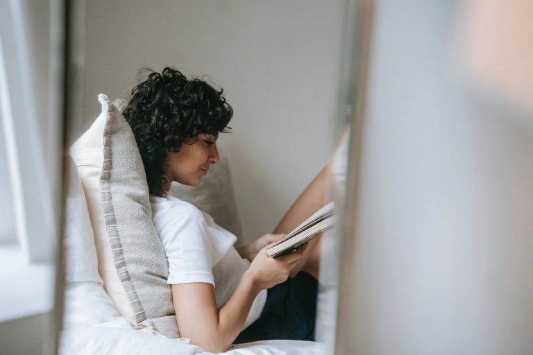 focused woman reading book on bed