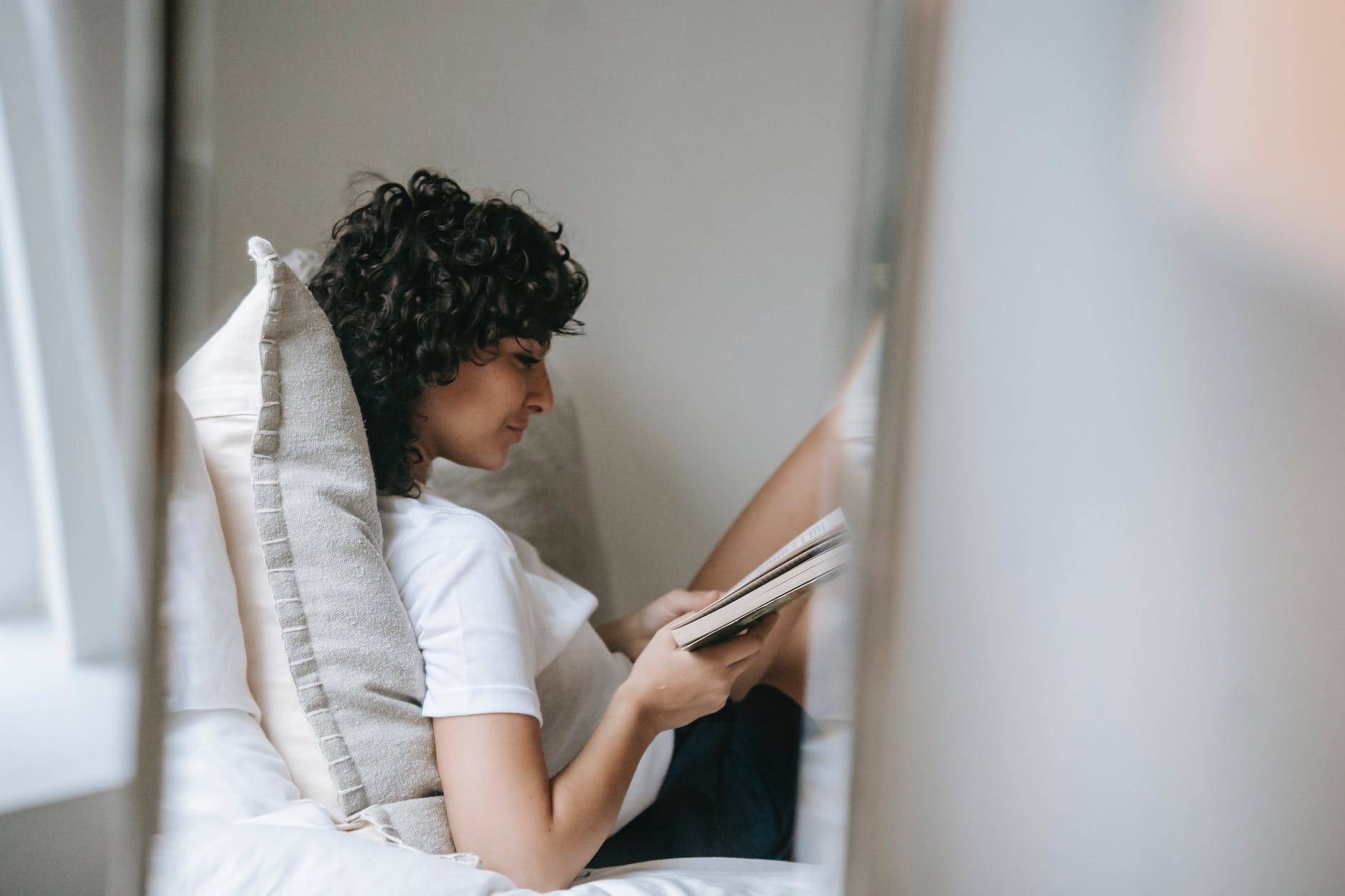 focused woman reading book on bed